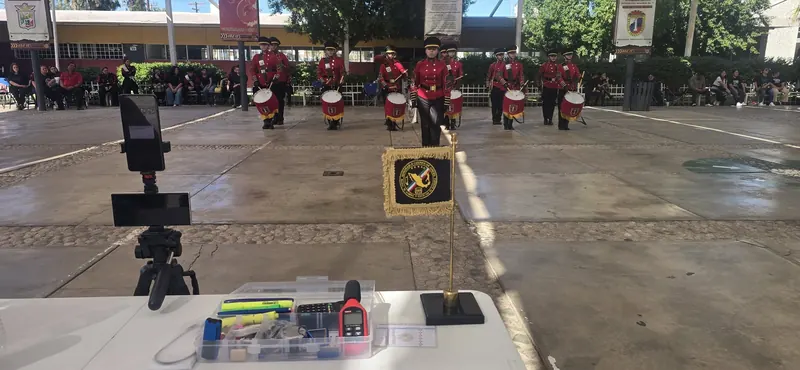 Mesa de jueceo con el banderín del Honorable Cuerpo de Jueces mientras una Banda de Guerra de uniforme rojo se presenta
